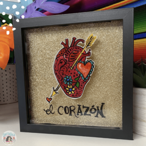 Reverse glass painting of human heart embellished with an arrow, typographic heart symbols, and flowers. The words el corazon painted underneath it.